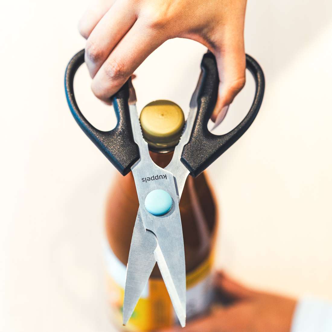 Eine Hand benutzt die Kuppels SELECTION Allzweckschere mit scharfen Klingen und integriertem Glasöffner, um einen verschlossenen Flaschenverschluss aufzudrehen.