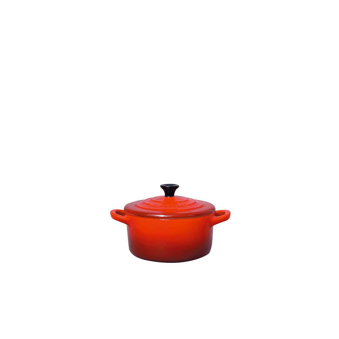 Eine kleine, runde, orange-rote Le Creuset SIGNATURE Mini Cocotte mit zwei seitlichen Griffen und einem schwarzen Knauf auf dem Deckel, ideal zum Servieren, steht mittig auf einem schlichten weißen Hintergrund.
