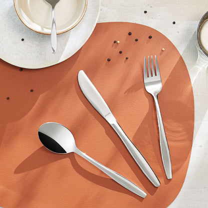 Das 24-teilige PONTIS Besteckset von Amefa aus hochglanzpoliertem Edelstahl 18/0 steht auf einem runden braunen Tischset mit Pfefferkörnern, daneben ein weißer Teller, eine kleine Schale und ein Glas Milch.