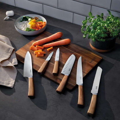 Das Kuppels WOOD Küchenmesser 2-teilig Set mit scharfer Klinge und Akazienholzgriff wird auf einem Holzschneidebrett mit geschnittenen Karotten, ganzen Karotten, gehacktem Gemüse in einer Schüssel, Kräutern in einem Topf und einem Küchentuch auf einer dunklen Arbeitsplatte präsentiert.