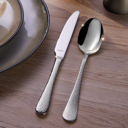 Ein strukturiertes Silbermesser und ein Löffel aus dem Kuppels Home CRYSTAL Besteckset 30-teilig liegen neben Keramiktellern auf einem Holztisch.