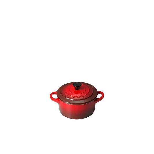 Eine kleine rote Le Creuset SIGNATURE Mini Cocotte mit zwei Griffen und einem schwarzen Knauf auf dem Deckel, perfekt zum Servieren, auf einem schlichten weißen Hintergrund.